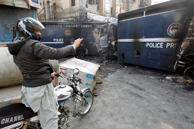 A passerby photographs police prison vans destroyed during clashes with protesters. (Reuters) A passerby photographs police prison vans destroyed during clashes with protesters. (Reuters)