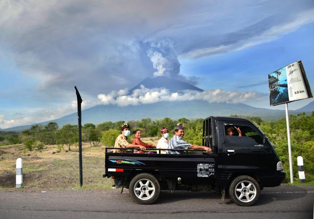 Balinese people ride on an open car past Mount Agung erupting seen from Kubu sub-district in Karangasem Regency, on Indonesia's resort island of Bali on November 27, 2017. (AFP) Balinese people ride on an open car past Mount Agung erupting seen from Kubu sub-district in Karangasem Regency, on Indonesia's resort island of Bali on November 27, 2017. (AFP)