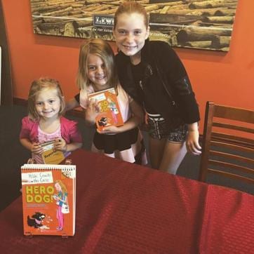 Hilde and her younger sisters with copies of her book, Hero Dog, a part of the Hilde Cracks the Case series. (Source: Hilde Lysiak)
