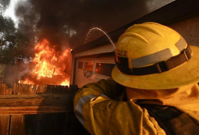 A Los Angeles County firefighter sprays water on a burning house in a wildfire in the Lake View Terrace area of Los Angeles. (AP Photo)
