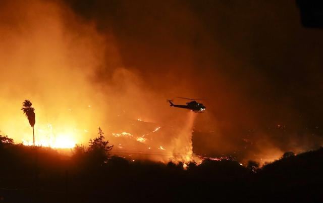 A helicopter drops water over a wildfire Thursday, Dec. 7, 2017, in Bonsall, Calif. The wind-swept blazes have forced tens of thousands of evacuations and destroyed dozens of homes in Southern California. (AP Photo)
