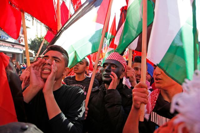 Palestinian youths protest with national flags near an Israeli checkpoint in the West Bank city of Ramallah on December 9, 2017. (AFP) Palestinian youths protest with national flags near an Israeli checkpoint in the West Bank city of Ramallah on December 9, 2017. (AFP)