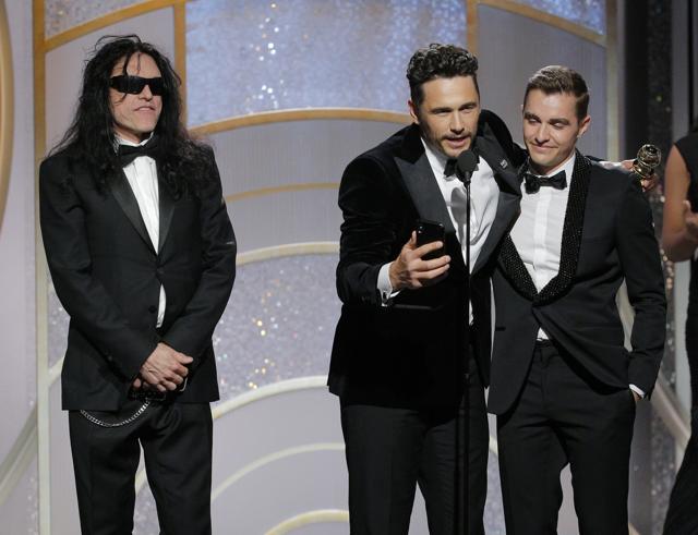 This image released by NBC shows James Franco, center, embracing his brother Dave Franco as he accepts the award for best actor in a motion picture comedy or musical for his role in The Disaster Artist, as Tommy Wiseau, left, looks on. (AP)