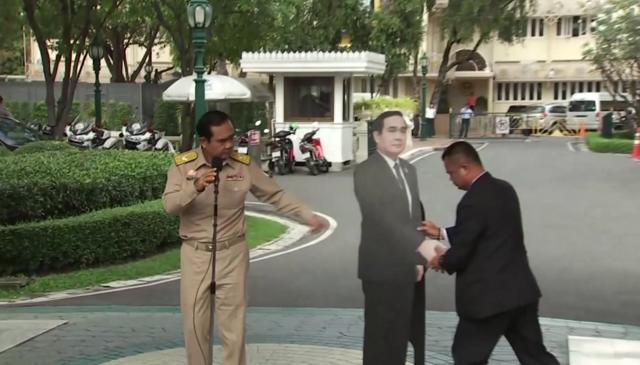 Prayuth Chan-ocha directs the scene as a life-sized cardboard cut-out figure of himself is carried into view by an aid, in Bangkok. (AP Photo)