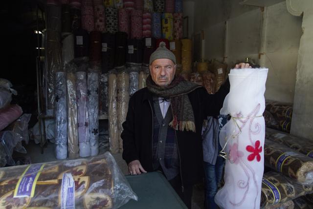 Mahmoud Mimeh, textile shops owner at the old market, poses for a picture inside his shop in the old city of Aleppo, Syria. (AP Photo)