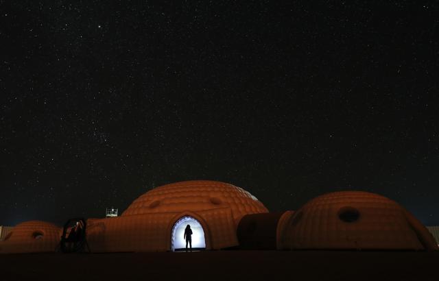 A member of the AMADEE-18 Mars simulation mission wearing a spacesuit standing in the doorway of a simulation habitat, with a view of the night sky above in Oman's Dhofar desert. (AFP Photo)