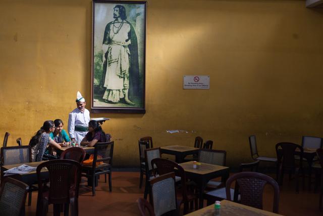 A waiter serves schoolgirls beneath a portrait of Rabindranath Tagore in the Indian Coffee House, Kolkata, India. (Courtesy: Tasveer )