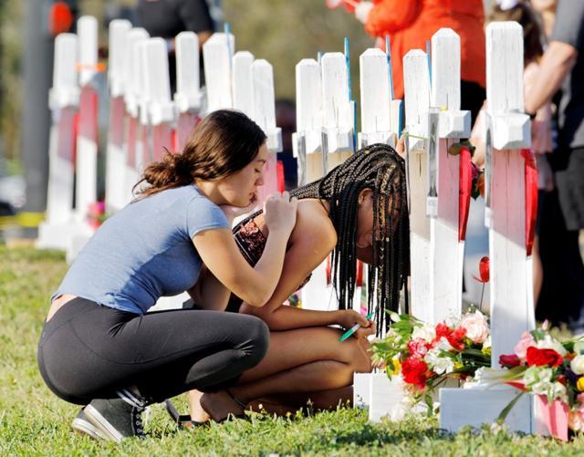 A senior at Marjory Stoneman Douglas High School weeps in front of a cross and Star of David for shooting victim Meadow Pollack while a fellow classmate consoles her at a memorial by the school in Parkland. (REUTERS) A senior at Marjory Stoneman Douglas High School weeps in front of a cross and Star of David for shooting victim Meadow Pollack while a fellow classmate consoles her at a memorial by the school in Parkland. (REUTERS)