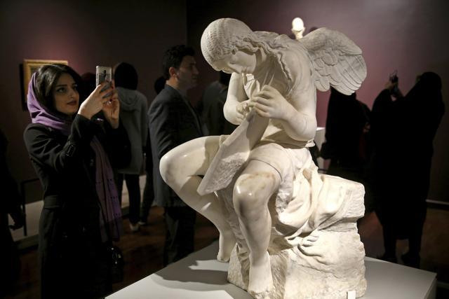 An Iranian woman takes a picture of a statue titled Funerary Genius in Tehran, Iran. (AP)