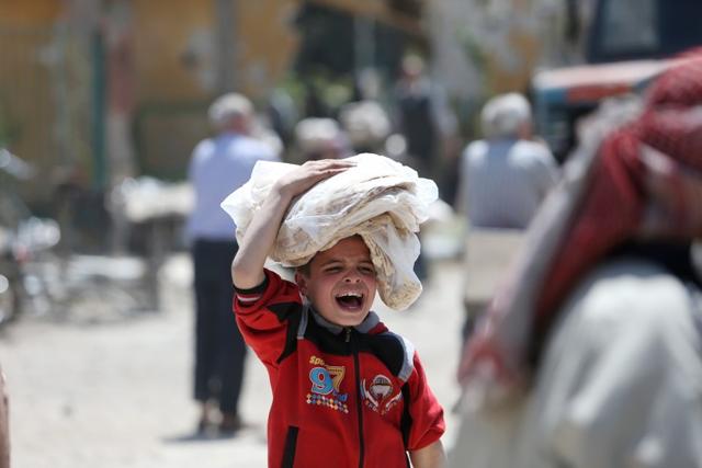 A boy gestures as he holds stacks of bread in Douma. (Reuters)