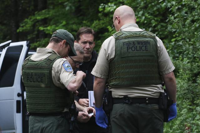 Washington State Fish and Wildlife Police confer with an individual from the King County Medical Examiner's and a King County Sheriff's deputy on a remote gravel road above Snoqualmie, WA., following a fatal cougar attack. (AP)