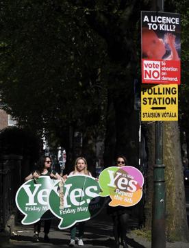 Women carry campaign placards in favour as they walk past a campaign poster against the repeal above a sign to a polling station on voting day in Ireland's referendum on the liberalisation of abortion law, in Dublin. (REUTERS) Women carry campaign placards in favour as they walk past a campaign poster against the repeal above a sign to a polling station on voting day in Ireland's referendum on the liberalisation of abortion law, in Dublin. (REUTERS)
