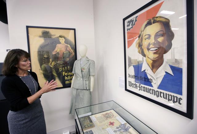 Sue Wilkins, director of education at The International Museum of World War II, in Natick, Mass., stands near a 1933 propaganda poster, right, that praised the Nazi organization German Labor Front, which was created after the Nazis eliminated trade unions. A mannequin, center, displays a uniform of the Nazi Lebensborn program, designed to be worn by women bearing children considered by the state as racially valuable. (AP) Sue Wilkins, director of education at The International Museum of World War II, in Natick, Mass., stands near a 1933 propaganda poster, right, that praised the Nazi organization German Labor Front, which was created after the Nazis eliminated trade unions. A mannequin, center, displays a uniform of the Nazi Lebensborn program, designed to be worn by women bearing children considered by the state as racially valuable. (AP)