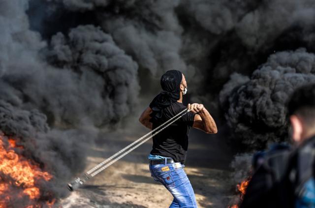 A Palestinian man uses a slingshot to throw a stone towards Israeli forces as smoke billows from burning tyres during a demonstration along the border with the Gaza strip east of Gaza city on June 1, 2018. (AFP Photo) A Palestinian man uses a slingshot to throw a stone towards Israeli forces as smoke billows from burning tyres during a demonstration along the border with the Gaza strip east of Gaza city on June 1, 2018. (AFP Photo)