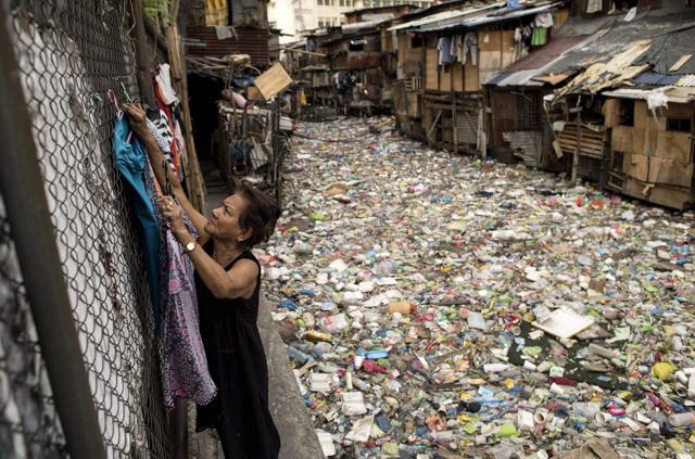 Perigrina Santos, 81, collects her laundry next to a garbage-filled creek in Manila. The blanket of trash on a creek that flows between the makeshift homes of a Manila slum is so dense it appears one could walk across it like a paved street. (AFP Photo)