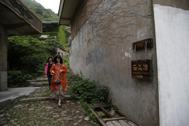 Tourists pass by a sign which reads Houtouwan. Some call it a "ghost village" which draws visitors down perilous footpaths winding past structures worn down by roots, rain, vines and wind. (AP) Tourists pass by a sign which reads Houtouwan. Some call it a "ghost village" which draws visitors down perilous footpaths winding past structures worn down by roots, rain, vines and wind. (AP)