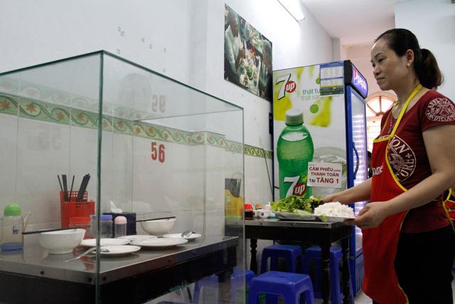 In this photograph taken on March 20, 2018, a waitress carries dishes to customers next to the glass-encased table where former US President Barack Obama sat at for a meal with chef Anthony Bourdain at Bun Cha Huong Lien restaurant, now dubbed "bun cha Obama", in Hanoi's old quarter. (AFP)
