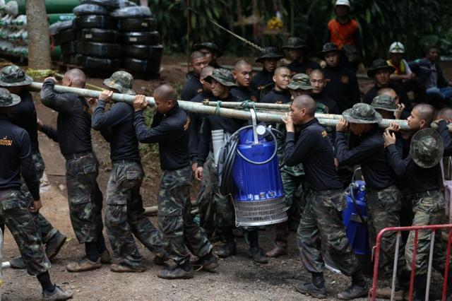 Military personnel carry a water pump machine as they enter the Tham Luang cave complex, where 12 boys and their soccer coach are trapped, in the northern province of Chiang Rai, Thailand, on Friday. (Reuters photo) Military personnel carry a water pump machine as they enter the Tham Luang cave complex, where 12 boys and their soccer coach are trapped, in the northern province of Chiang Rai, Thailand, on Friday. (Reuters photo)