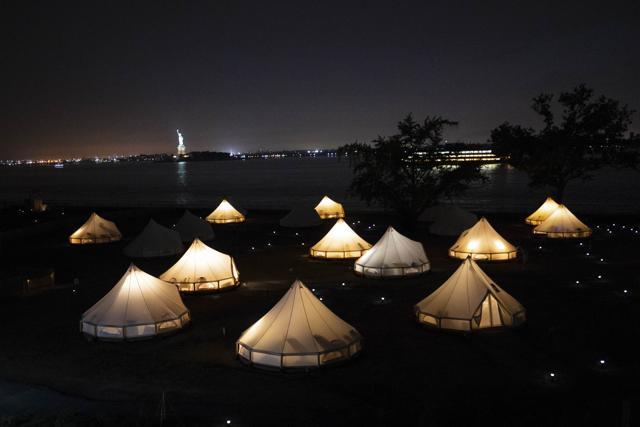 Glowing journey tents at night against the Statue of Liberty and the Staten Island Ferry. (David Gray/Bloomberg) Glowing journey tents at night against the Statue of Liberty and the Staten Island Ferry. (David Gray/Bloomberg)