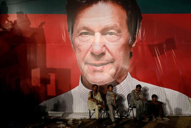 Workers, who set up the venue, sit under a wall with a billboard displaying photo of Imran Khan, chairman of the Pakistan Tehreek-e-Insaf (PTI), political party, as they listen to him during a campaign rally ahead of general elections in Karachi. (Reuters Photo) Workers, who set up the venue, sit under a wall with a billboard displaying photo of Imran Khan, chairman of the Pakistan Tehreek-e-Insaf (PTI), political party, as they listen to him during a campaign rally ahead of general elections in Karachi. (Reuters Photo)