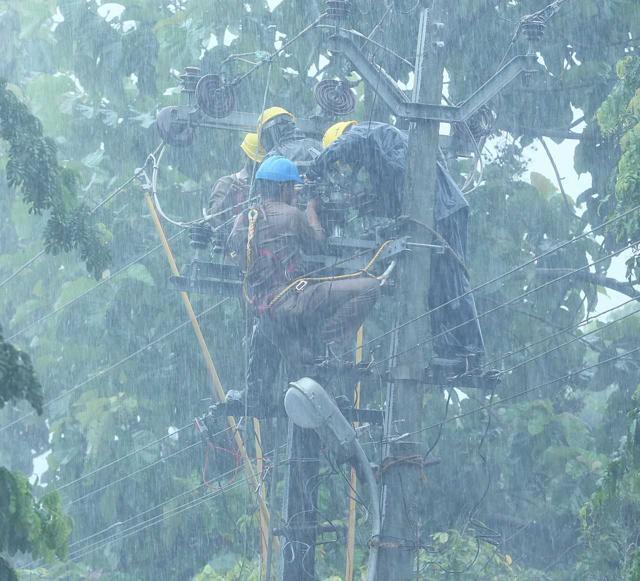 Local workmen fix an electric pole during a torrential downpour in Kannur district. (HT Photo) Local workmen fix an electric pole during a torrential downpour in Kannur district. (HT Photo)