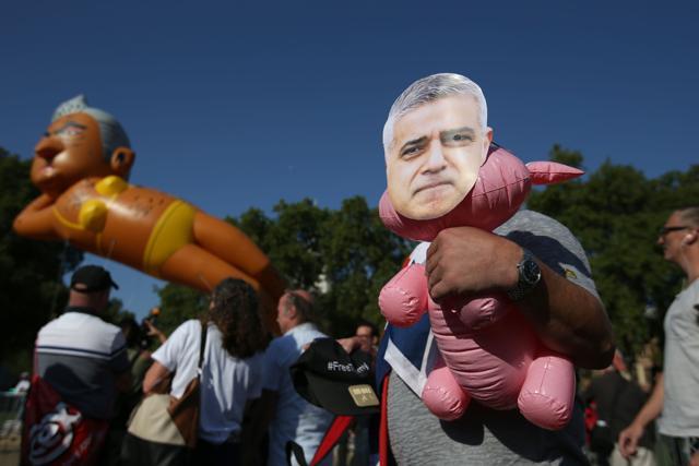 A demonstrator holds an inflatable toy with a mask of London Mayor Sadiq Khan as a large balloon depicting London Mayor Sadiq Khan in a yellow bikini floats over demonstrators. (AFP) A demonstrator holds an inflatable toy with a mask of London Mayor Sadiq Khan as a large balloon depicting London Mayor Sadiq Khan in a yellow bikini floats over demonstrators. (AFP)