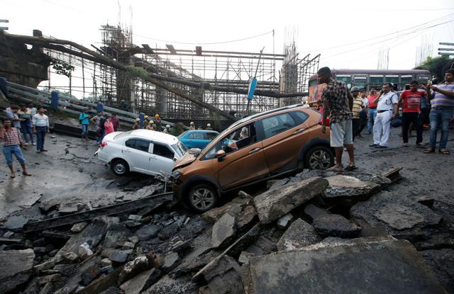 People stand next to the wreckage of vehicles at the site of a bridge that collapsed in Kolkata. (Reuters Photo) People stand next to the wreckage of vehicles at the site of a bridge that collapsed in Kolkata. (Reuters Photo)