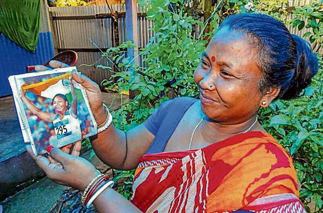 Swapna’s mother Basana Barman, holds up a picture of her daughter at the Games. Basana often did double shifts plucking leaves at a tea garden, after her husband suffered a stroke, to provide for him and their four children. (PTI) Swapna’s mother Basana Barman, holds up a picture of her daughter at the Games. Basana often did double shifts plucking leaves at a tea garden, after her husband suffered a stroke, to provide for him and their four children. (PTI)