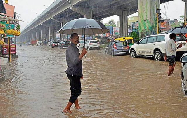 A man crossing the waterlogged Chandigarh-Ambala road near Patiala chowk in Zirakpur on Monday. Traffic moved at a snail’s pace for hours. (HT Photo)