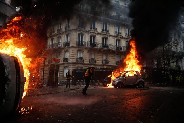 Protesters walk by burning cars during clashes with riot police on the sideline of a protest of Yellow vests (Gilets jaunes) against rising oil prices and living costs, on December 1, 2018 in Paris. (AFP) Protesters walk by burning cars during clashes with riot police on the sideline of a protest of Yellow vests (Gilets jaunes) against rising oil prices and living costs, on December 1, 2018 in Paris. (AFP)