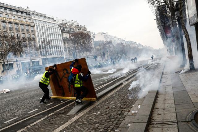 Protesters wearing yellow vests (gilets jaunes) protect themselves from tear gas with a wooden board in the middle of a street during a demonstration against rising costs of living they blame on high taxes near the Arc de Triomphe on the Champs-Elysees avenue in Paris, on December 8, 2018. (AFP Photo) Protesters wearing yellow vests (gilets jaunes) protect themselves from tear gas with a wooden board in the middle of a street during a demonstration against rising costs of living they blame on high taxes near the Arc de Triomphe on the Champs-Elysees avenue in Paris, on December 8, 2018. (AFP Photo)