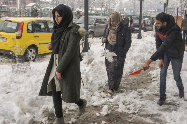 Srinagar: A shopkeeper clears snow in front of his shop as women walk past at Lal Chowk, in Srinagar, Saturday, Jan. 05, 2019. According to the MeT department officials, most places in Kashmir, including plains of the valley, received moderate to heavy snowfall overnight. (PTI) Srinagar: A shopkeeper clears snow in front of his shop as women walk past at Lal Chowk, in Srinagar, Saturday, Jan. 05, 2019. According to the MeT department officials, most places in Kashmir, including plains of the valley, received moderate to heavy snowfall overnight. (PTI)