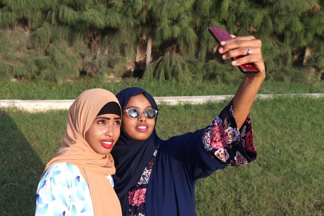 (FILES) In this file photograph taken on November 4, 2018, Rahma Abdullahi Mohamud (R) and Hani Hussein take selfies pictures with a mobile phone, after buying clothes designed by fashion designer Muna Mohamed Abdullahi, at Peace Garden in Mogadishu, Somalia. (Photo by Abdi HAJJI HUSSEIN / AFP) (AFP) (FILES) In this file photograph taken on November 4, 2018, Rahma Abdullahi Mohamud (R) and Hani Hussein take selfies pictures with a mobile phone, after buying clothes designed by fashion designer Muna Mohamed Abdullahi, at Peace Garden in Mogadishu, Somalia. (Photo by Abdi HAJJI HUSSEIN / AFP) (AFP)