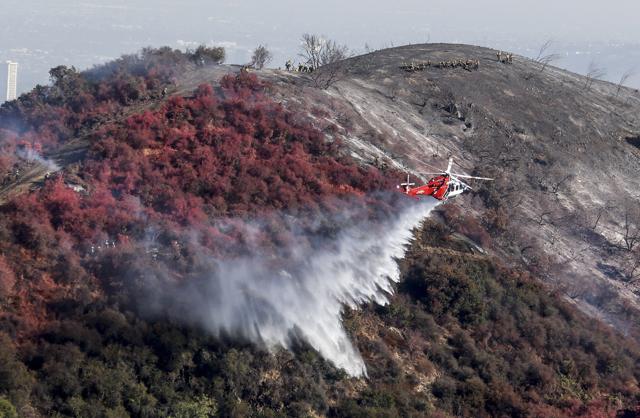 A helicopter drops water as a wildfire called the Getty fire burns on Kenter Canyon in Los Angeles. (AP) A helicopter drops water as a wildfire called the Getty fire burns on Kenter Canyon in Los Angeles. (AP)
