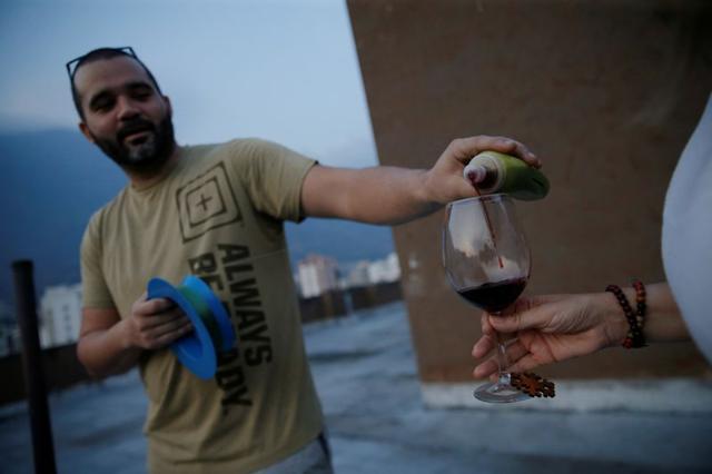 Un hombre llena la copa de un vecino en un techo con vino durante una cuarentena a nivel nacional debido al coronavirus.  (REUTERS)