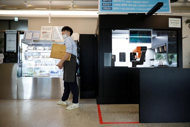An employee stands next to a barista robot. (REUTERS) An employee stands next to a barista robot. (REUTERS)
