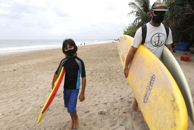 Tourists wearing face masks carry their surfboard at Kuta beach, Bali, Indonesia on Thursday, July 9, 2020. Indonesia's resort island of Bali reopened after a three-month virus lockdown Thursday, allowing local people and stranded foreign tourists to resume public activities before foreign arrivals resume in September. (AP) Tourists wearing face masks carry their surfboard at Kuta beach, Bali, Indonesia on Thursday, July 9, 2020. Indonesia's resort island of Bali reopened after a three-month virus lockdown Thursday, allowing local people and stranded foreign tourists to resume public activities before foreign arrivals resume in September. (AP)