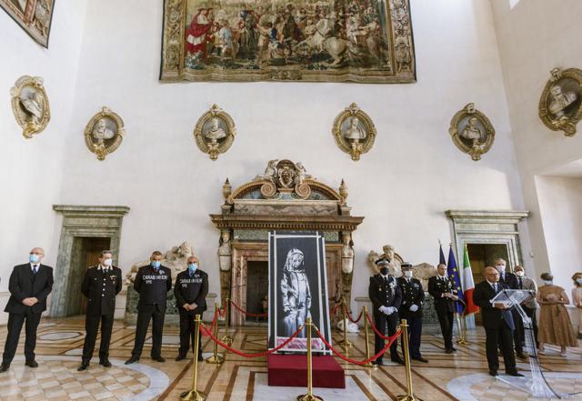 A recovered stolen artwork by British artist Banksy, depicting a young female figure with a mournful expression, that was painted as a tribute to the victims of the 2015 terror attacks at the Bataclan music hall in Paris, is returned to the French Ambassador to Italy, Christian Masset, fourth from right, during a ceremony at the French Embassy in Rome, Tuesday, July 14, 2020. (AP) A recovered stolen artwork by British artist Banksy, depicting a young female figure with a mournful expression, that was painted as a tribute to the victims of the 2015 terror attacks at the Bataclan music hall in Paris, is returned to the French Ambassador to Italy, Christian Masset, fourth from right, during a ceremony at the French Embassy in Rome, Tuesday, July 14, 2020. (AP)