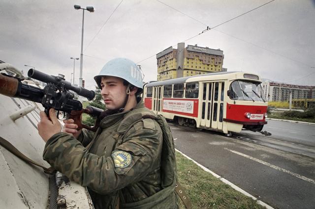 FILE - In this Sunday, March 27, 1994, file photo, a Ukrainian U.N. soldier holds a weapon while protecting a tram diving through the so called Snipers Alley, in Sarajevo, Bosnia, backdropped by the Holiday Inn hotel. The Holiday Hotel, which opened as Holiday Inn, a luxurious accommodation for world's royalty, film stars and other dignitaries who came to watch the 1984 Winter Olympics, and less than a decade later, became ground zero of the bloody siege of Sarajevo in the 1990's. (AP) FILE - In this Sunday, March 27, 1994, file photo, a Ukrainian U.N. soldier holds a weapon while protecting a tram diving through the so called Snipers Alley, in Sarajevo, Bosnia, backdropped by the Holiday Inn hotel. The Holiday Hotel, which opened as Holiday Inn, a luxurious accommodation for world's royalty, film stars and other dignitaries who came to watch the 1984 Winter Olympics, and less than a decade later, became ground zero of the bloody siege of Sarajevo in the 1990's. (AP)