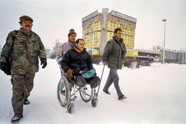 FILE - In this Tuesday, Feb. 15, 1994 file photo, three wounded Bosnian war veterans, walking with the aid of artificial limbs and pushing a legless comrade in a wheelchair, venture down one of Sarajevo's deadliest roads, called Sniper Alley, walking by the Holiday Inn hotel in Sarajevo, Bosnia. The Holiday Hotel, which opened as Holiday Inn, a luxurious accommodation for world's royalty, film stars and other dignitaries who came to watch the 1984 Winter Olympics, and less than a decade later, became ground zero of the bloody siege of Sarajevo in the 1990's. (AP) FILE - In this Tuesday, Feb. 15, 1994 file photo, three wounded Bosnian war veterans, walking with the aid of artificial limbs and pushing a legless comrade in a wheelchair, venture down one of Sarajevo's deadliest roads, called Sniper Alley, walking by the Holiday Inn hotel in Sarajevo, Bosnia. The Holiday Hotel, which opened as Holiday Inn, a luxurious accommodation for world's royalty, film stars and other dignitaries who came to watch the 1984 Winter Olympics, and less than a decade later, became ground zero of the bloody siege of Sarajevo in the 1990's. (AP)