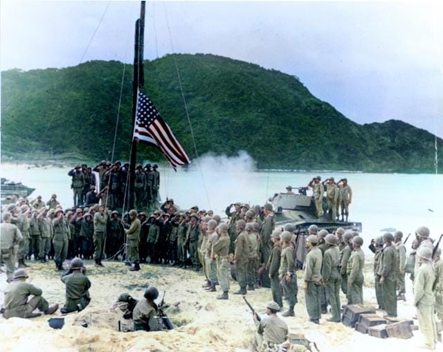 In this black and white photo digitally colorized and published in 2020 by Anju Niwata and Hidenori Watanave, U.S. Army and Coast Guardsmen stand at attention as the American flag is raised over Akashima, Japan on April 2, 1945, the little island, only a few miles from Okinawa. (AP) In this black and white photo digitally colorized and published in 2020 by Anju Niwata and Hidenori Watanave, U.S. Army and Coast Guardsmen stand at attention as the American flag is raised over Akashima, Japan on April 2, 1945, the little island, only a few miles from Okinawa. (AP)