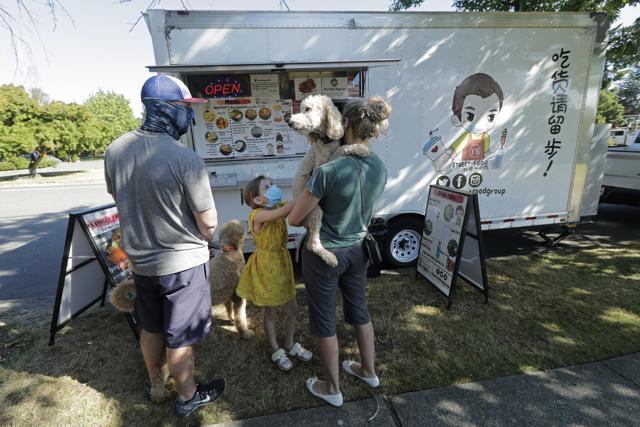 Bobby Price, left, and Catherine Vogt, right, stand with Catherine's daughter Avery, 8, and their dogs as they wait to order from the YS Street Food food truck, Monday, Aug. 10, 2020, near the suburb of Lynnwood, Wash., north of Seattle. (AP)
