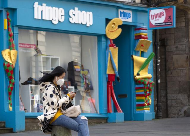A woman scans her smartphone outside the Fringe Shop on the Royal Mile in Edinburgh, Scotland Friday Aug. 21, 2020. (AP)