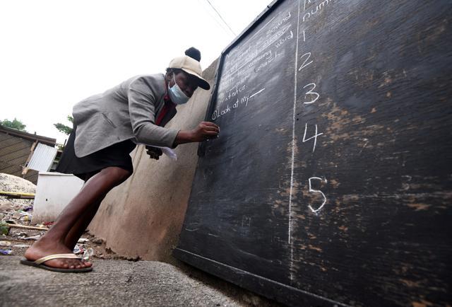 Educator Taneka Mckoy Phipps writes a lesson on a blackboard painted on a zinc fence in Jamaica. (REUTERS) Educator Taneka Mckoy Phipps writes a lesson on a blackboard painted on a zinc fence in Jamaica. (REUTERS)