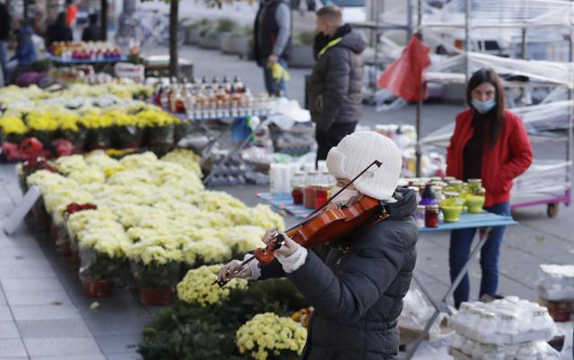 A woman plays the violin near to people buying flowers, after Poland's government closed all cemeteries in an attempt to curb the spread of COVID-19, in Warsaw, Poland. (AP) A woman plays the violin near to people buying flowers, after Poland's government closed all cemeteries in an attempt to curb the spread of COVID-19, in Warsaw, Poland. (AP)