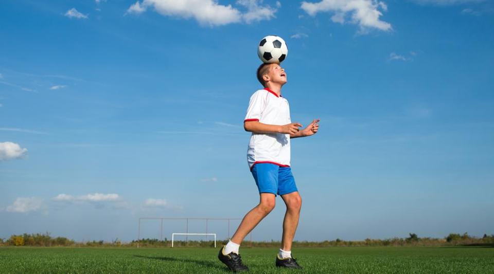 Ребенок с футбольным мячом. Прыжки на одной ноге футбол дети. Мальчик пинает мяч фото. Соседи футболисты над головой.
