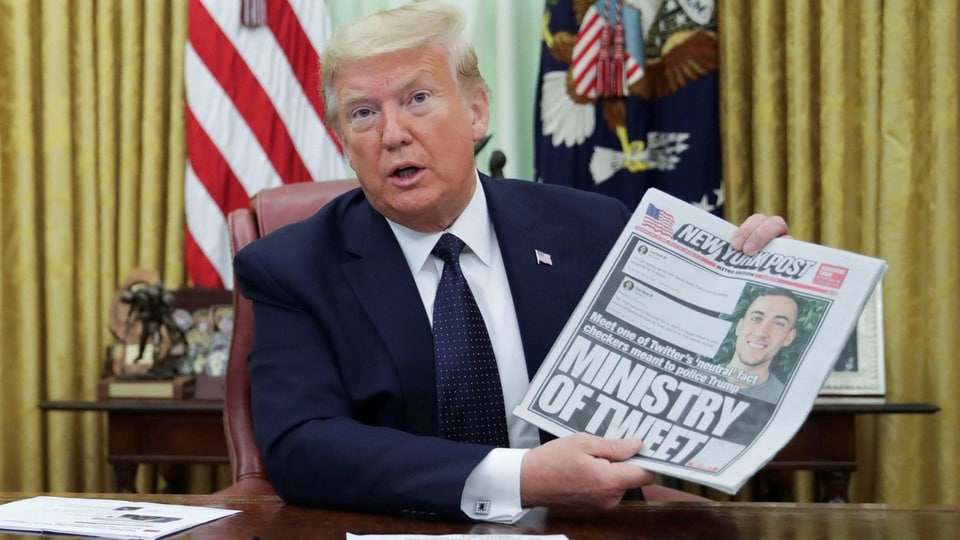 U.S. President Donald Trump holds up a front page of the New York Post as he speaks to reporters while signing an executive order on social media companies in the Oval Office of the White House in Washington