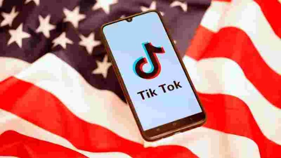 TikTok logo is displayed on the smartphone while standing on the U.S. flag in this illustration.