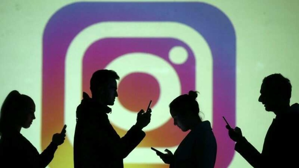 Silhouettes of mobile users are seen next to a screen projection of the Instagram logo in this picture illustration taken March 28, 2018. REUTERS/Dado Ruvic/Illustration