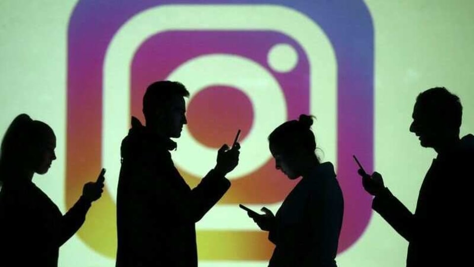 Silhouettes of mobile users are seen next to a screen projection of the Instagram logo in this picture illustration taken March 28, 2018. REUTERS/Dado Ruvic/Illustration/File Photo